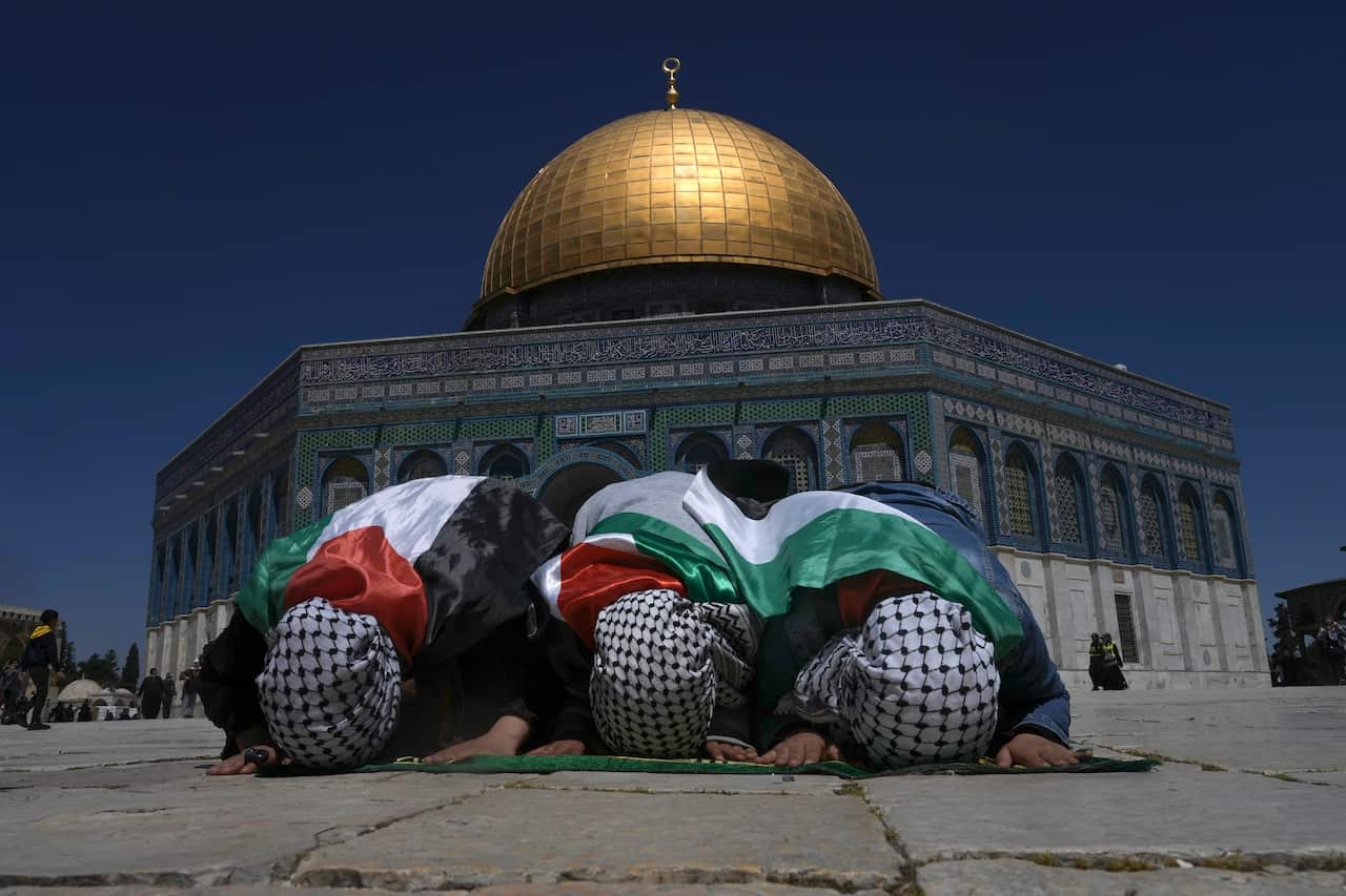 Muslim worshippers wrapped in the Palestinian flags pray during holy Islamic month of Ramadan in front of the Dome of the Rock shrine at the Al Aqsa Mosque compound in Jerusalem's Old City, Friday, April 15, 2022. Palestinians clashed with Israeli police 