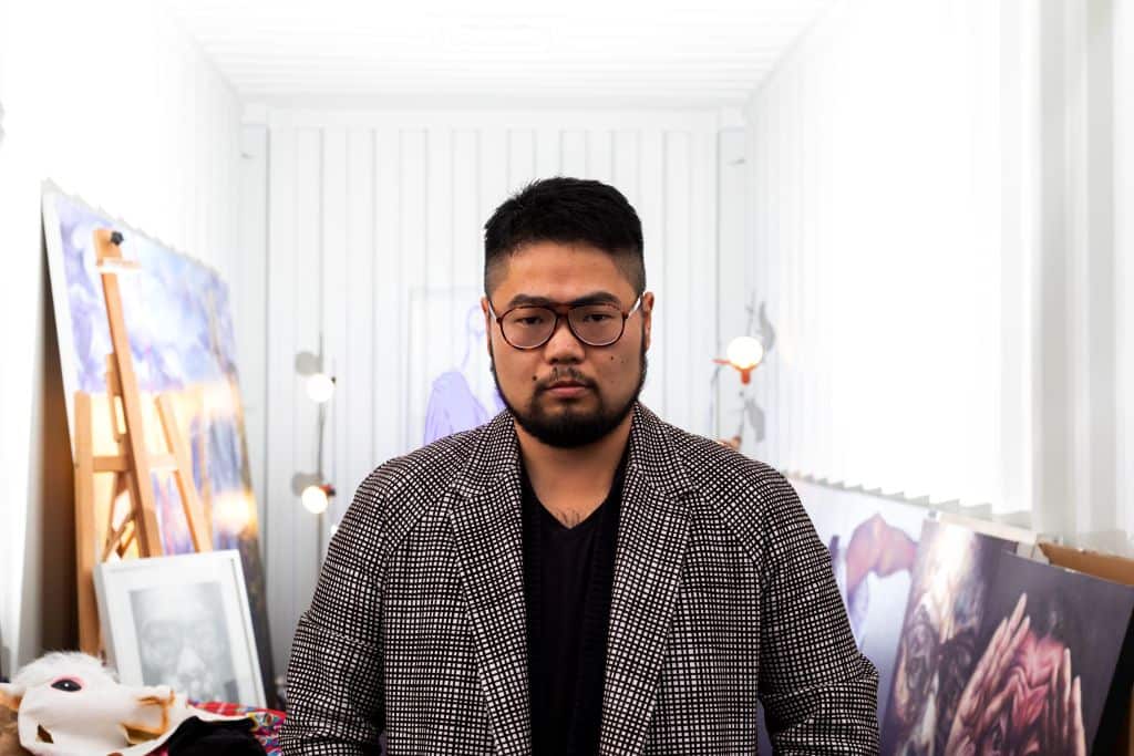 Chinese cartoonist Badiucao standing behind his artwork titled 'Light' in his studio in Melbourne.