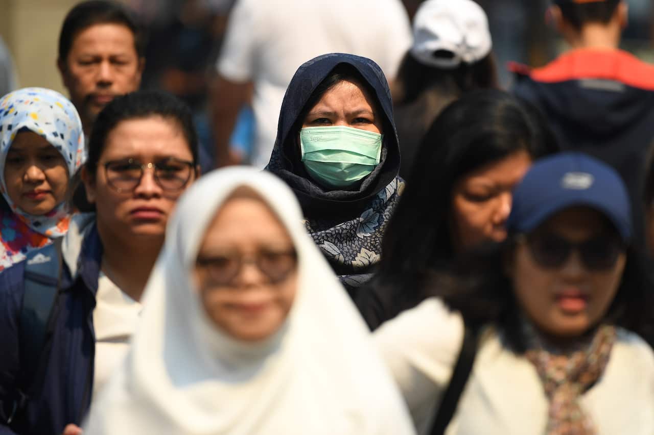 A woman seen wearing a dust mask as smoke haze from bushfires in New South Wales blankets the CBD in Sydney, Tuesday, December 3, 2019. (AAP Image/Joel Carrett) NO ARCHIVING