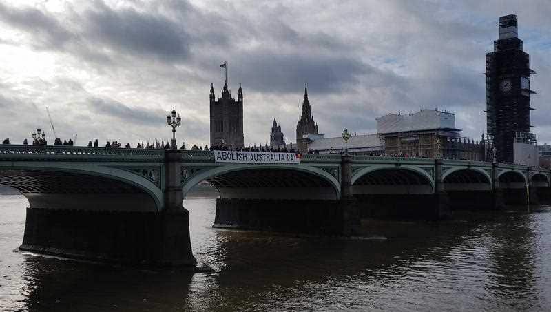 Anti-Australia Day protesters hold a banner saying "Abolish Australia Day" over the side of the Westminster Bridge.