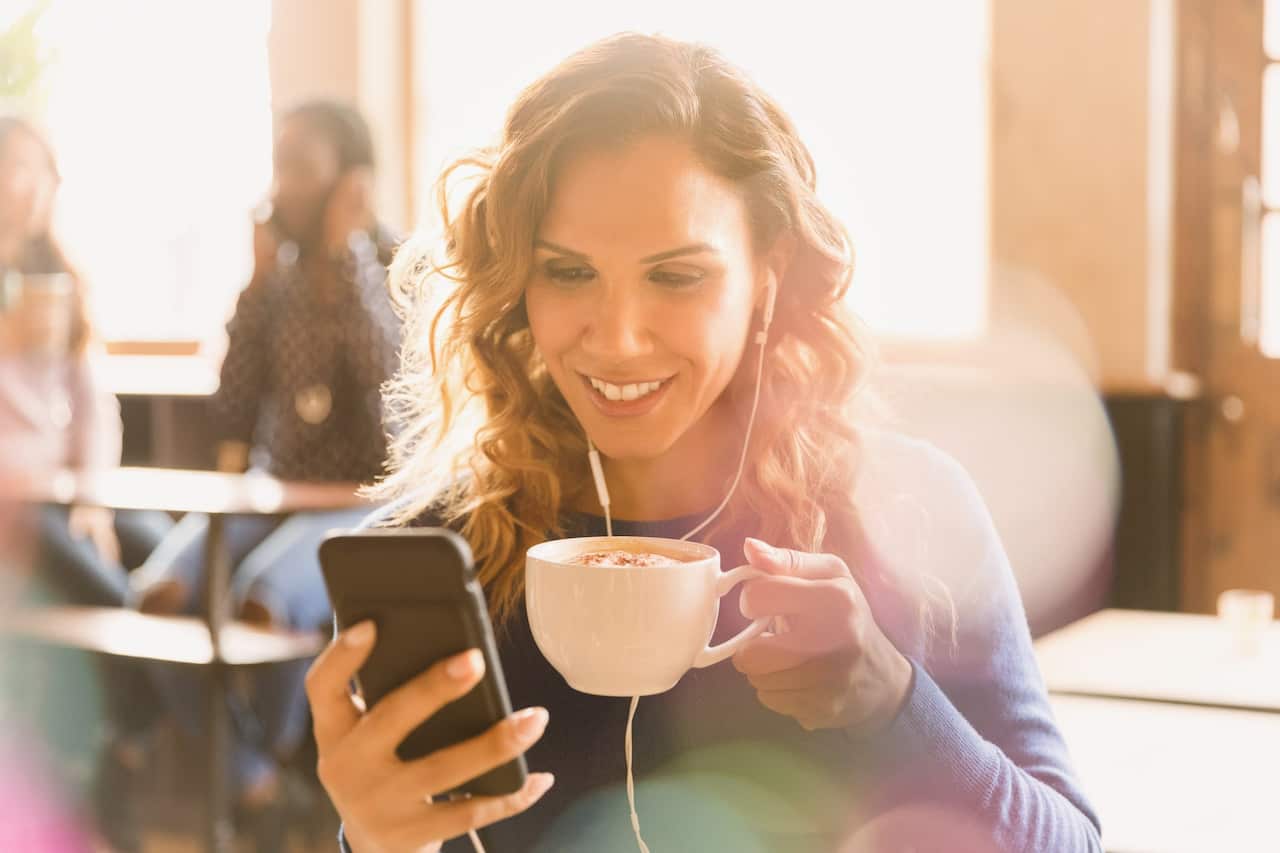 Woman with headphones drinking cappuccino and video chatting in cafe