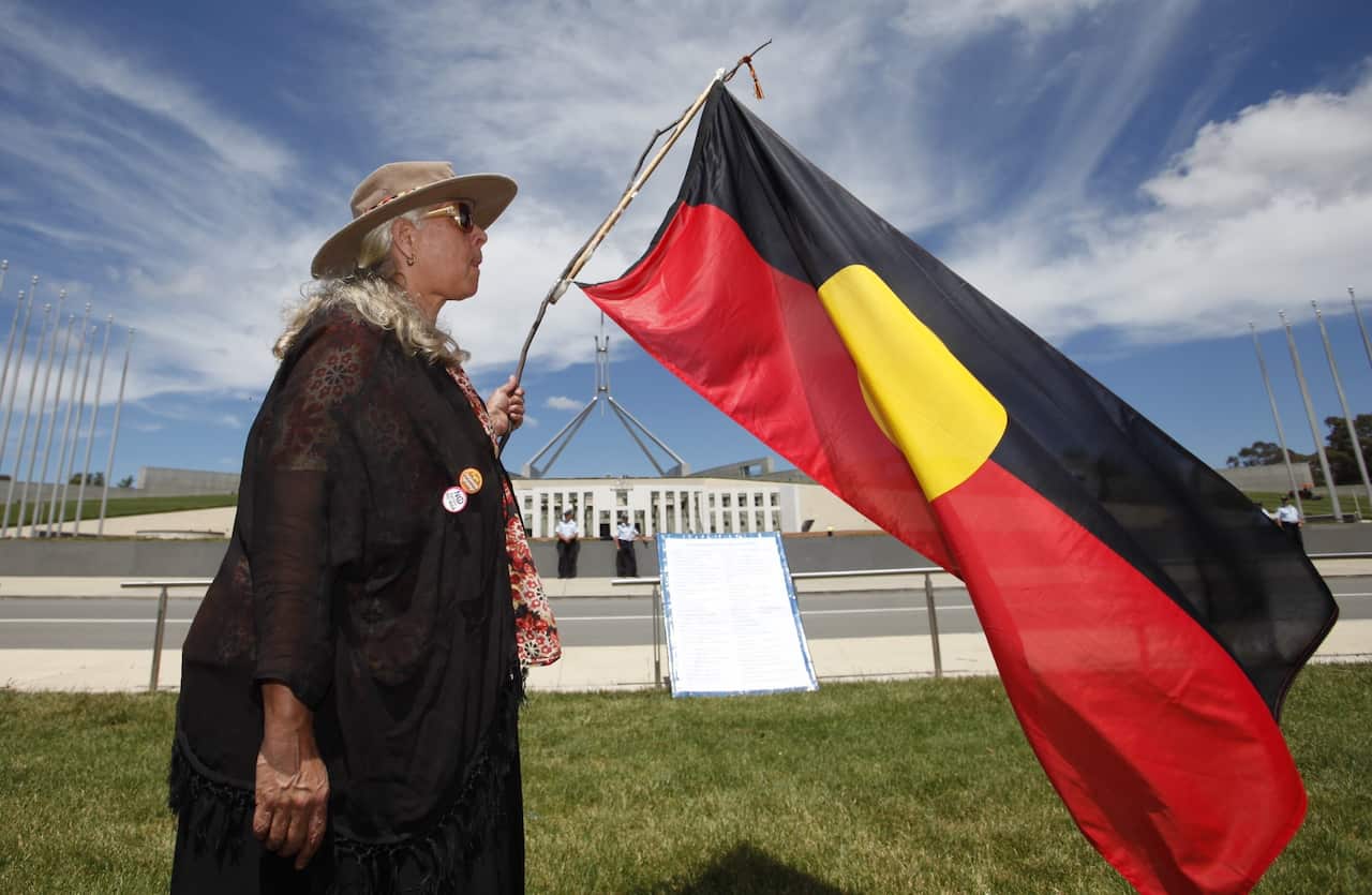 A woman holds an Australian Aboriginal flag in front of the Parliament House in Canberra