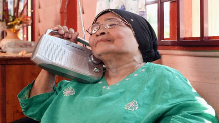 An elderly woman listening to the radio.
