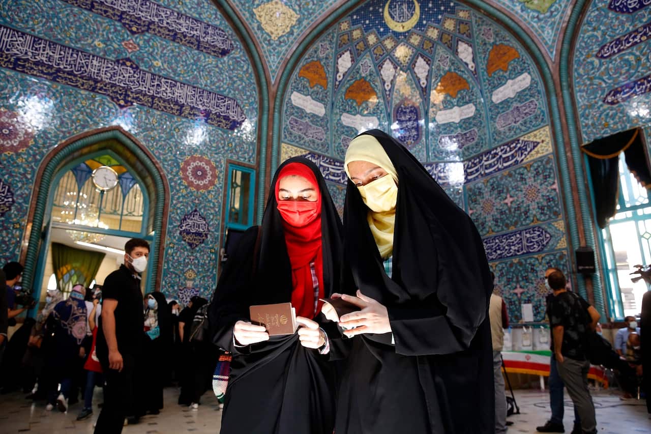 Two Iranian women check their ID papers to cast their votes at a polling station during the presidential election in Tehran, Iran.