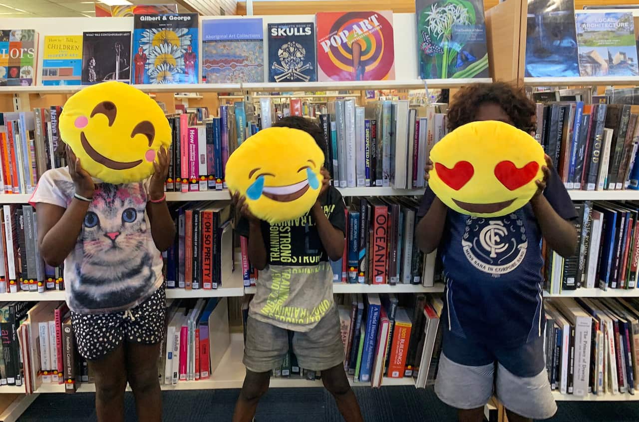 Aboriginal kids in Alice Springs librar holding emoji plush toys in front of their faces
