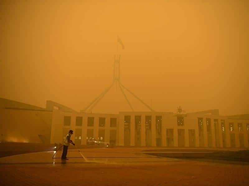A man cleans Parliament House's forecourt surrounded by smoke haze