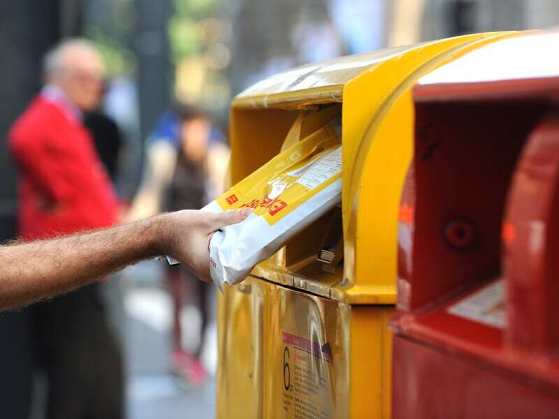 A man posting mail at an Australia Post postbox in Sydney