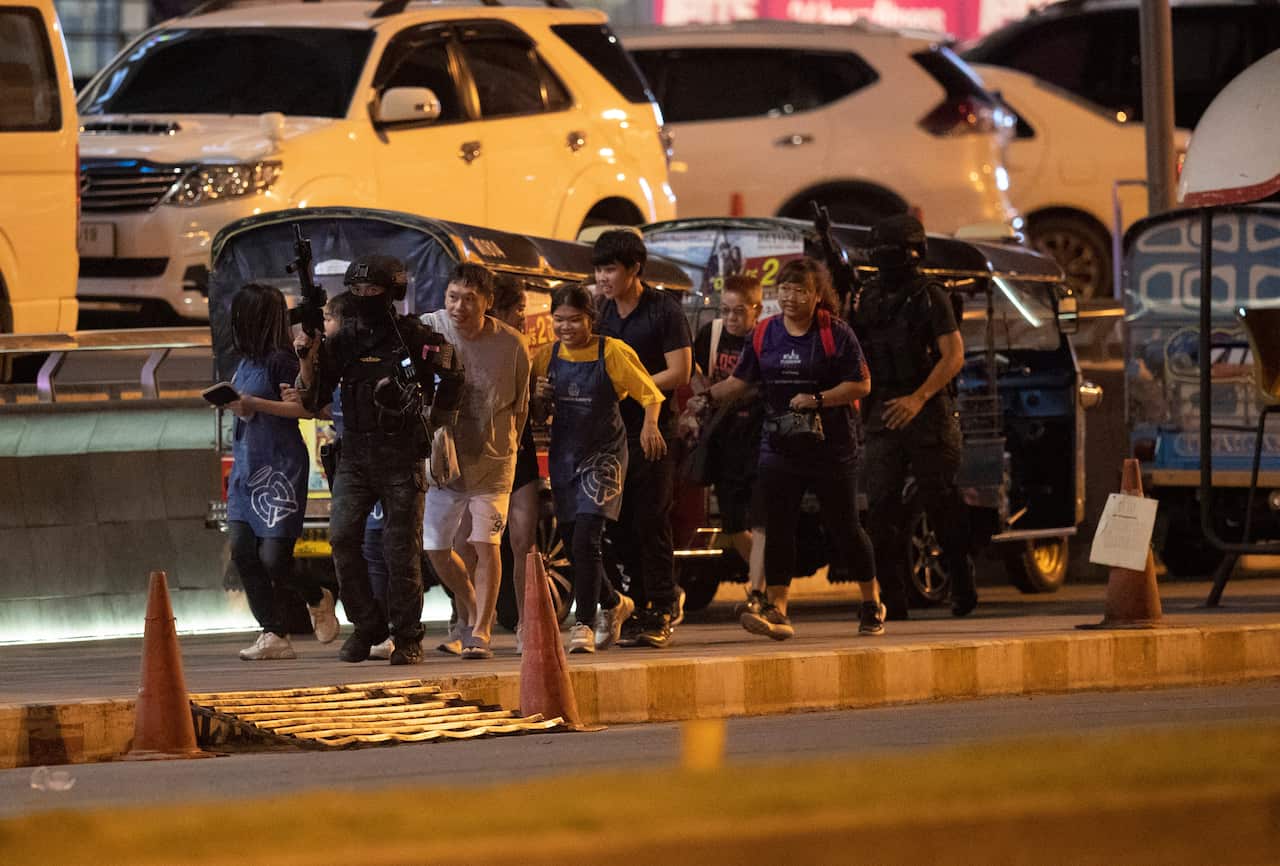 People who were able to get out of Terminal 21 Korat mall are escorted outside by armed commando soldiers.