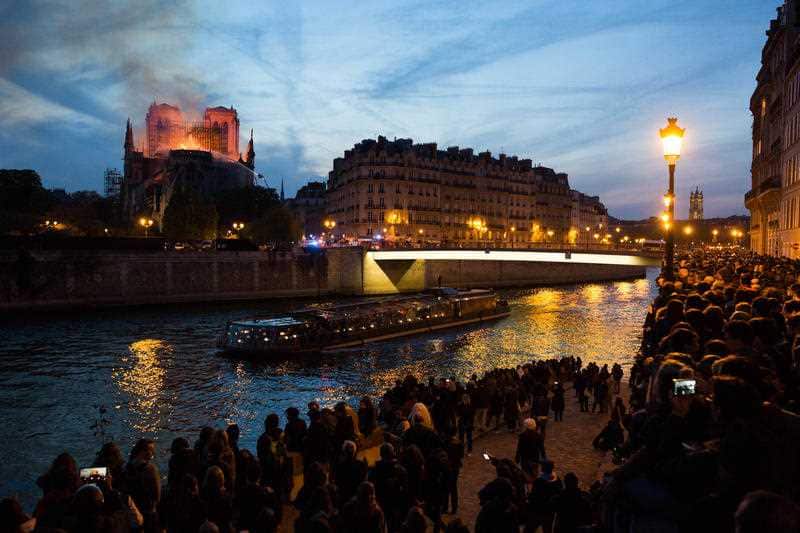 Bystanders look on as flames and smoke are seen billowing from the roof at Notre-Dame Cathedral.