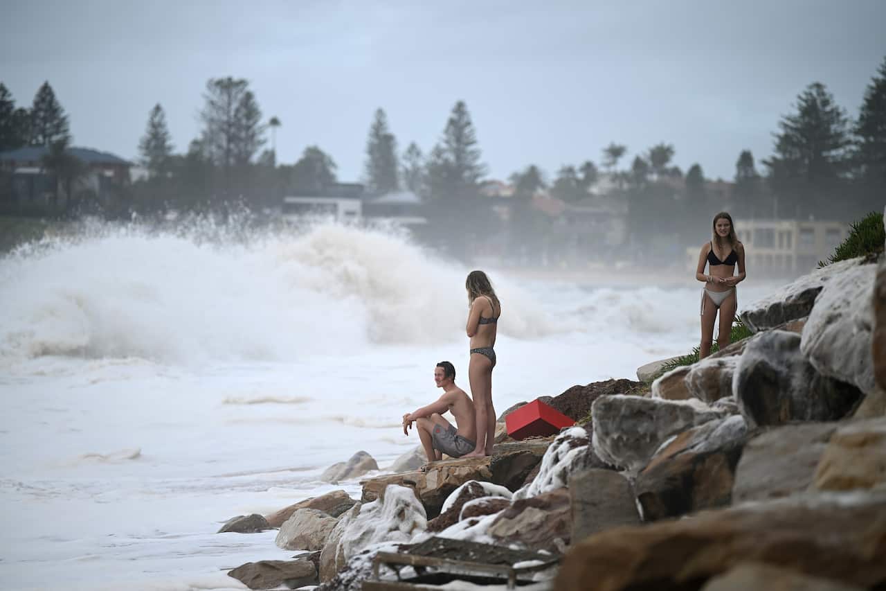 Swimmer watch from the rocks as sea foam brought by waves approaches Collaroy.