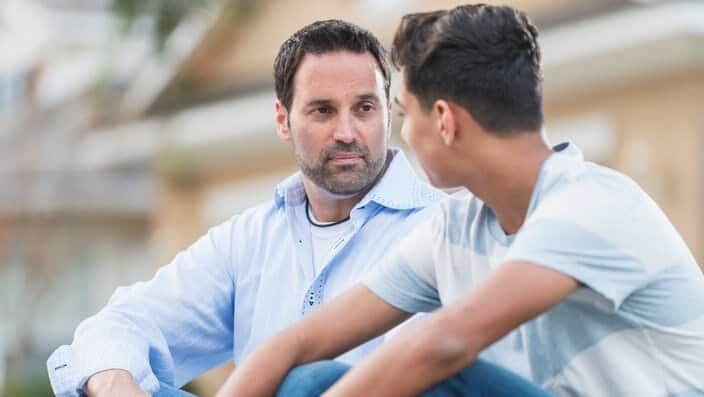 Father sitting with serious teenage boy