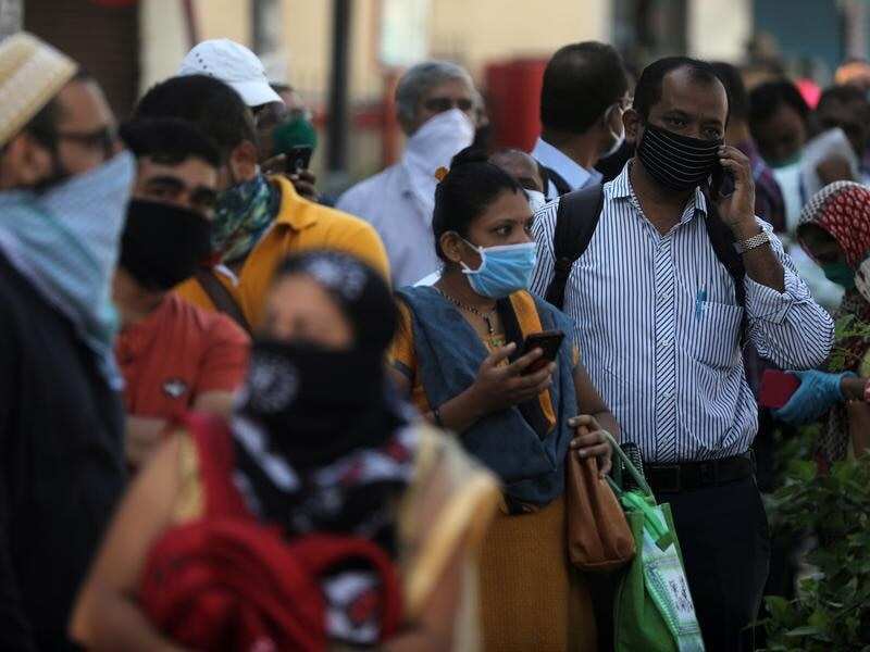People wait in a queue to board a public bus in Mumbai