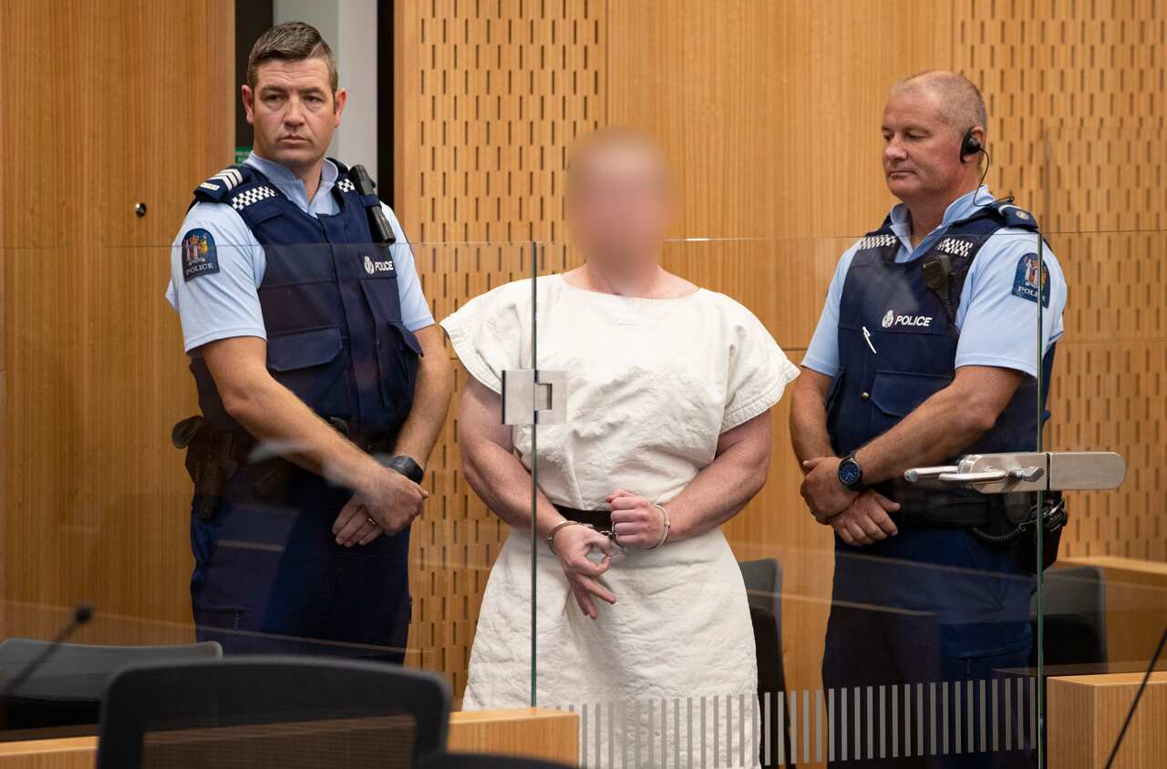 The man accused of carrying out the Christchurch mosque murders makes a sign to cameras during his court appearance.