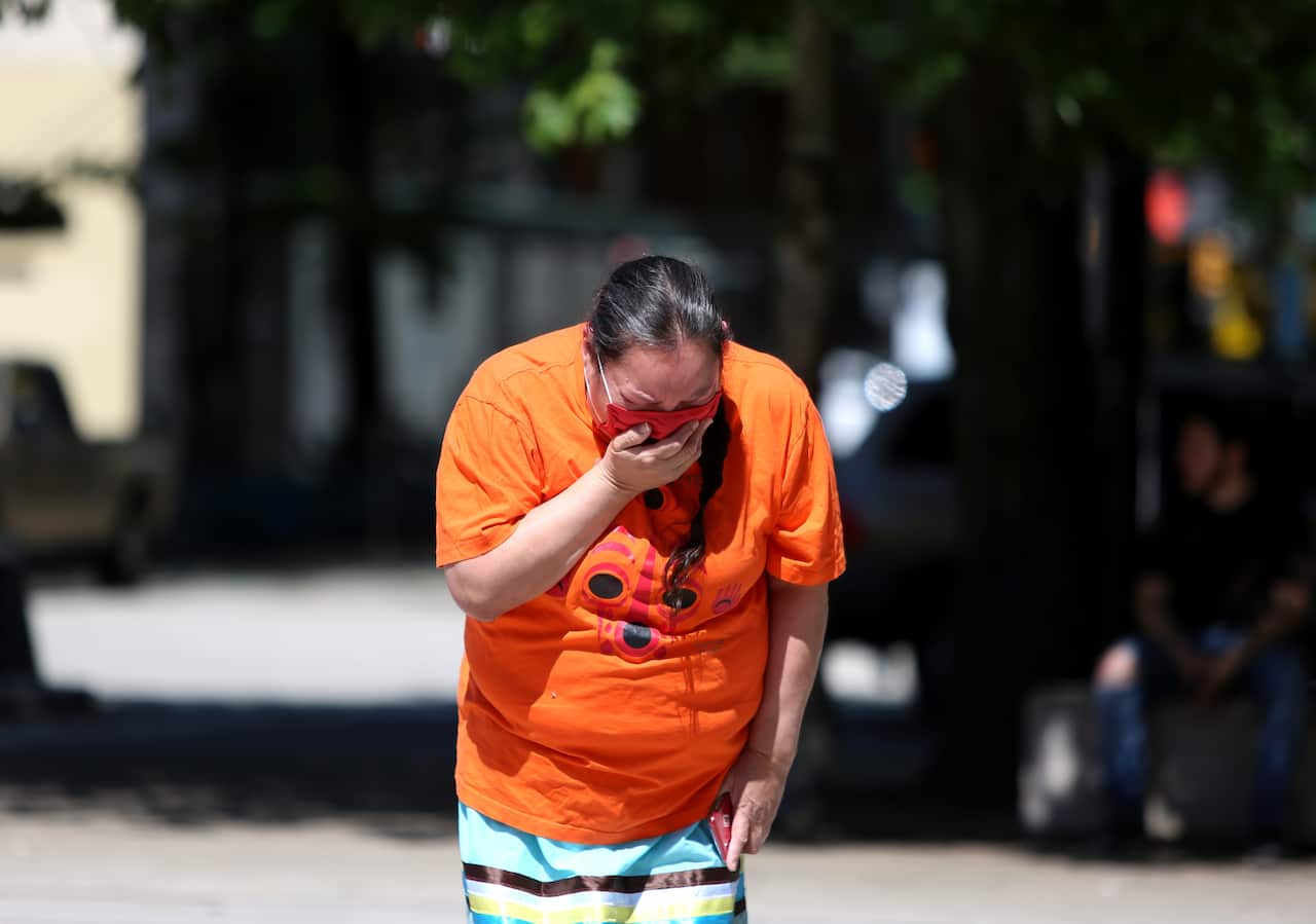 A woman mourns over 215 pairs of kids shoes  outside Vancouver Art Gallery during a memorial on 29 May, 2021 in Vancouver, British Columbia, Canada.