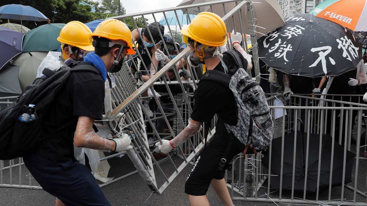 Protesters with umbrellas use steel barricades to block a road as they march through Sha Tin District in Hong Kong.