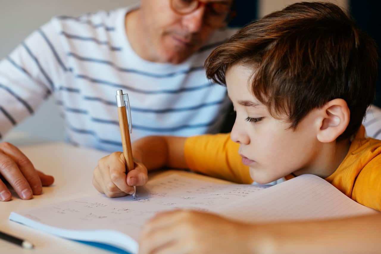 Father watching son doing homework at table