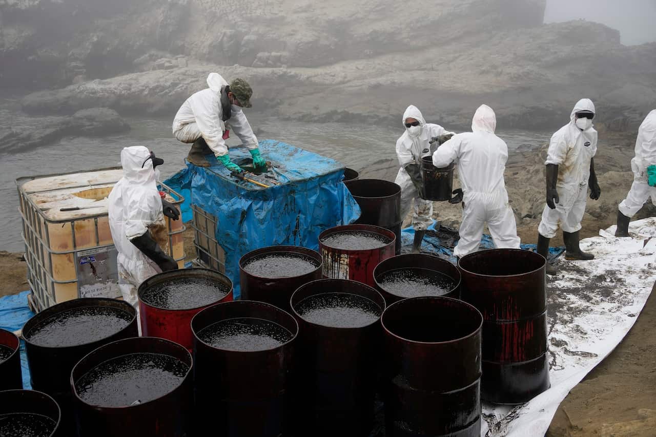 Workers clean oil from Cavero Beach after a spill in Ventanilla, Peru.