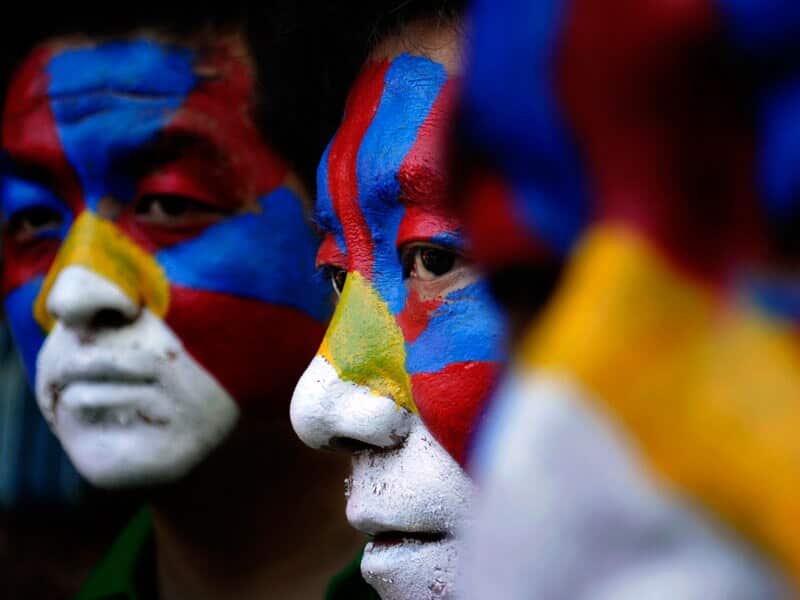Tibetan people with faces painted in the Tibetan flag colours.