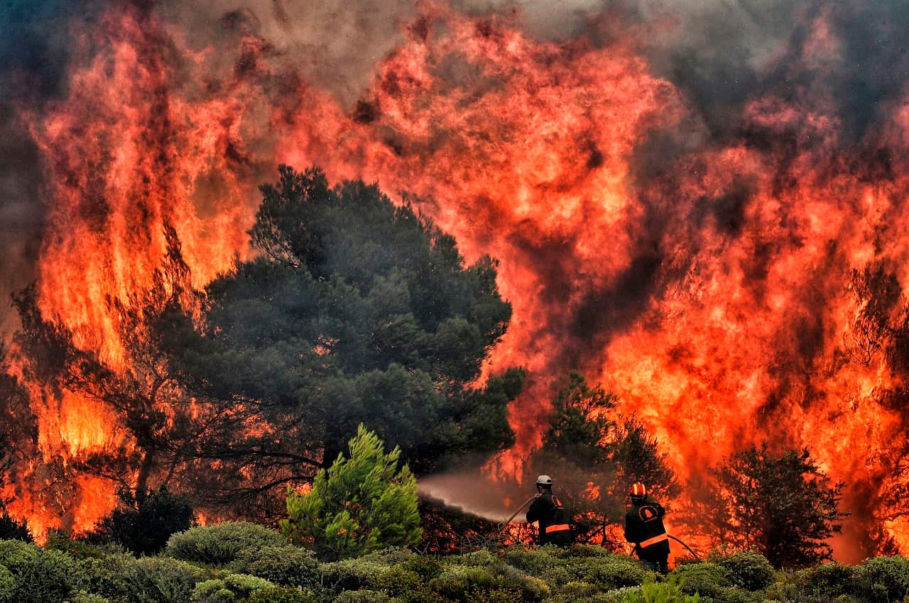 Firefighters try to extinguish flames during a wildfire at the village of Kineta.