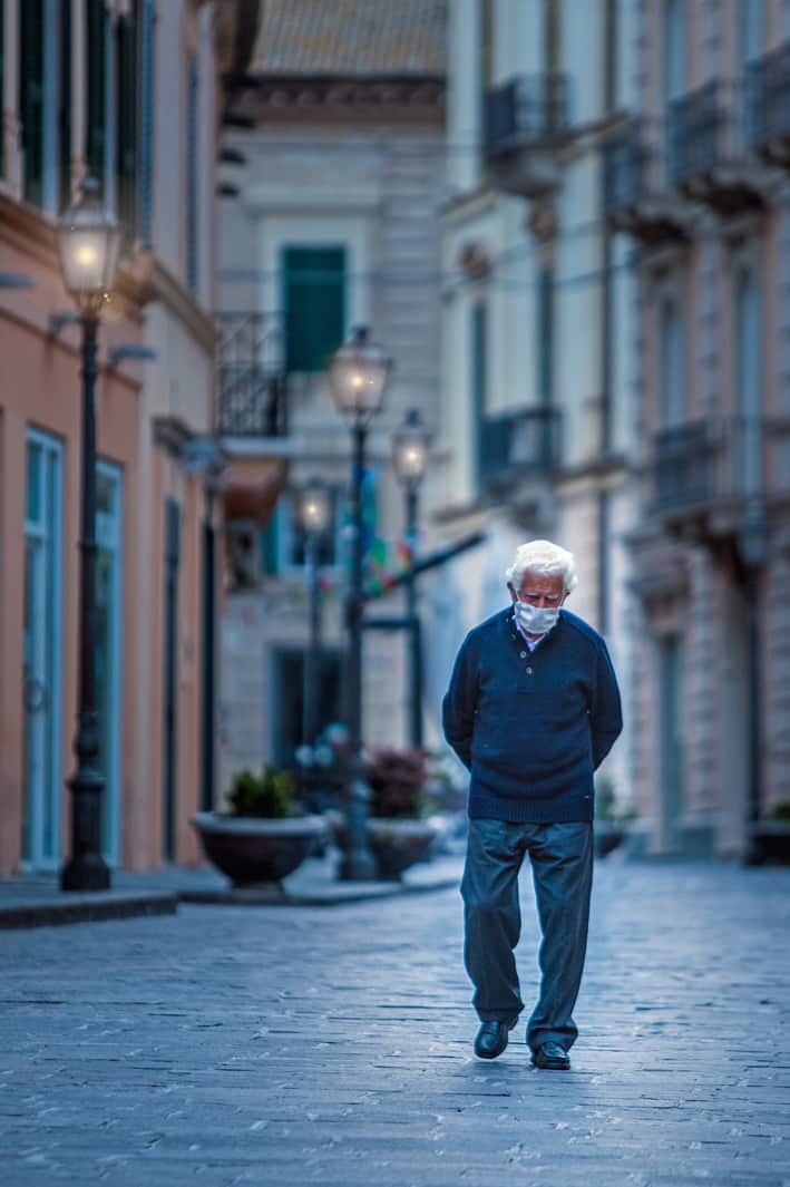 An old man walking alone wearing a face mask