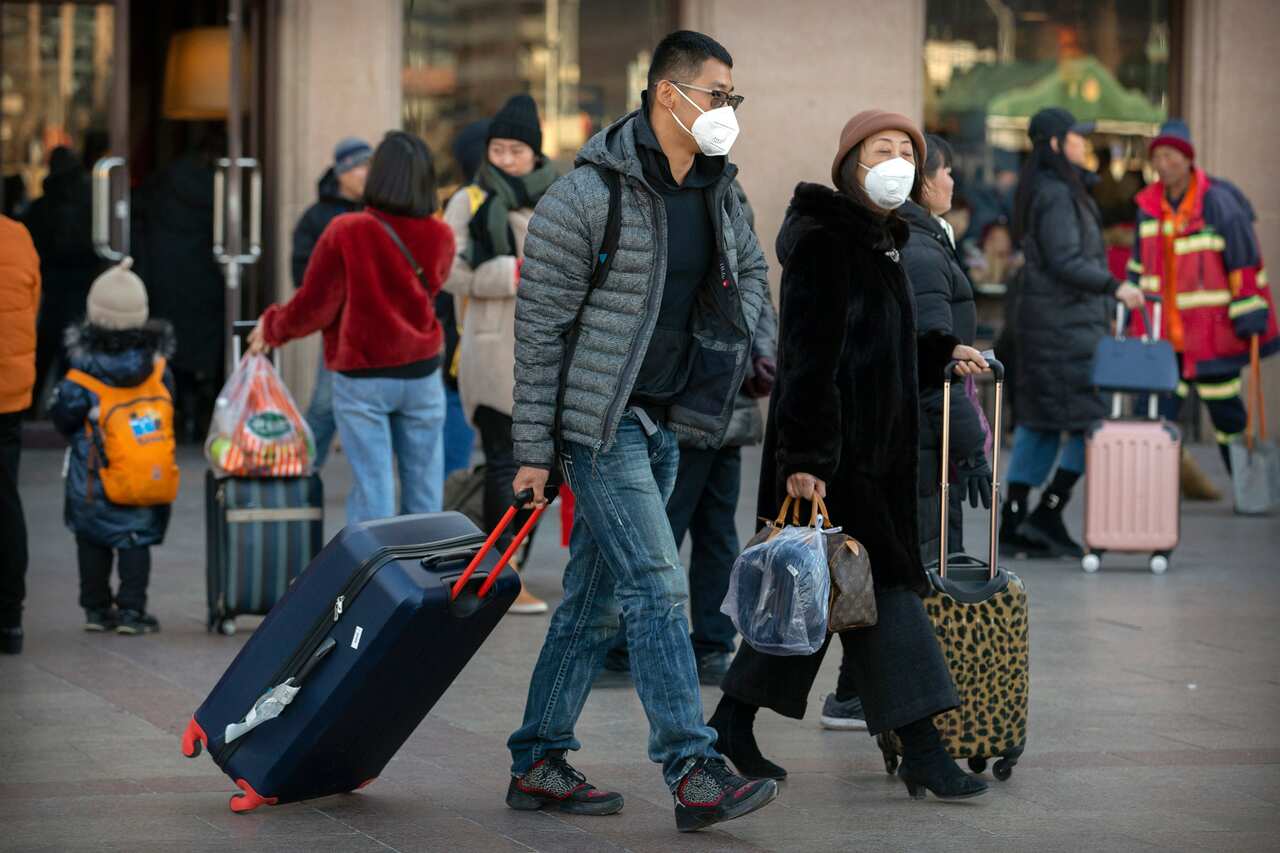 Travelers wear face masks as they walk outside of the Beijing Railway Station in Beijing.