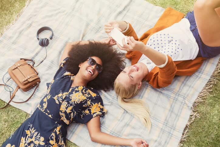 Friends taking selfie relaxing on blanket in grass