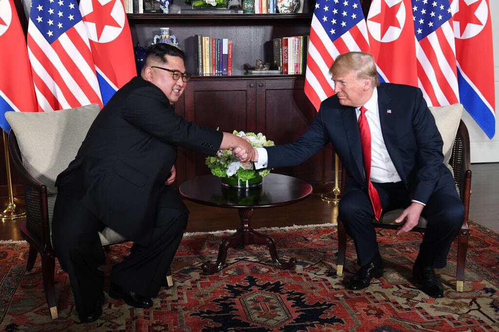 Donald Trump (R) shakes hands with North Korea's leader Kim Jong Un (L) as they sit down for their historic US-North Korea summit.