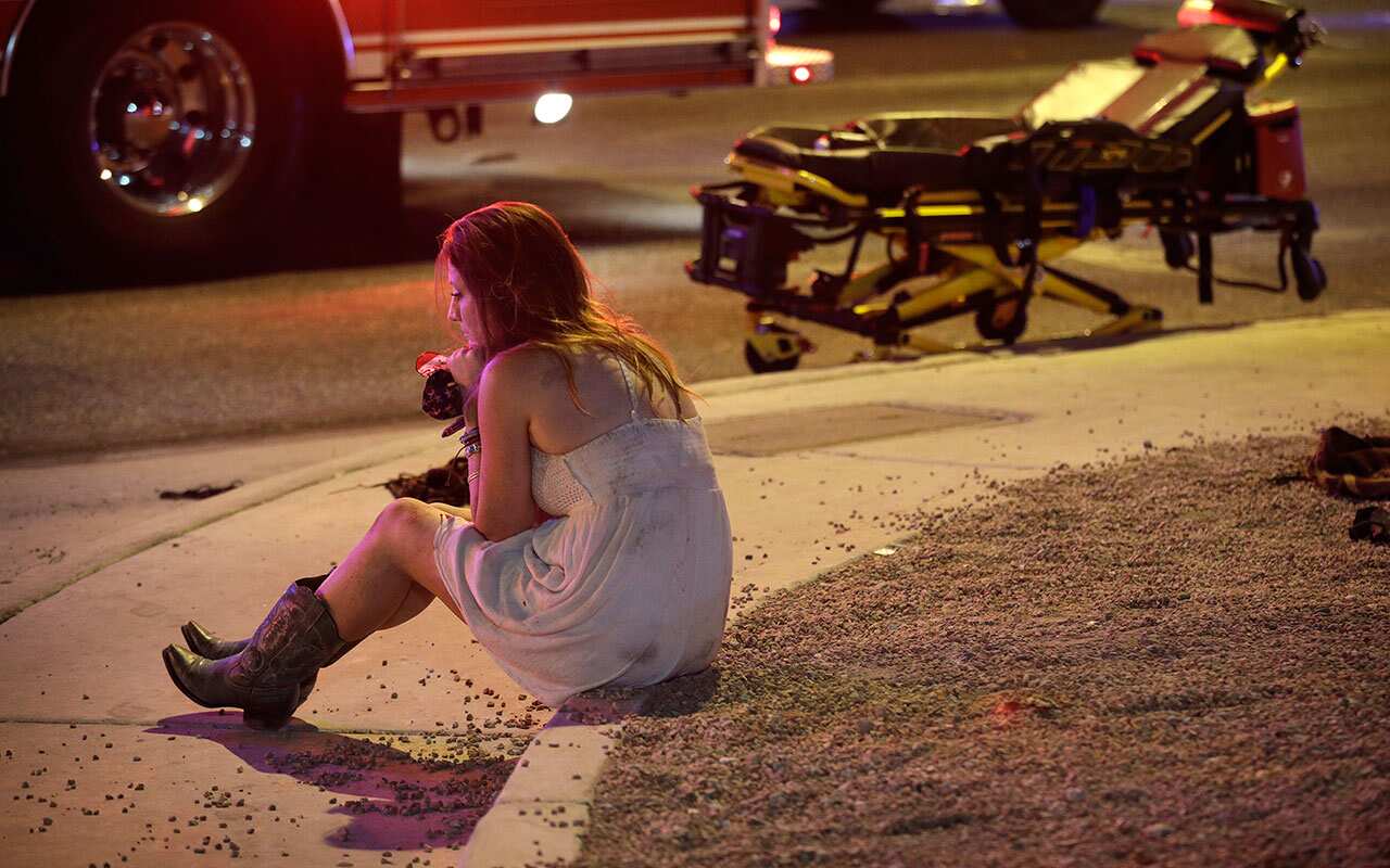 A woman sits on a curb at the scene of a shooting outside of a music festival along the Las Vegas Strip, Monday, Oct. 2, 2017, in Las Vegas.