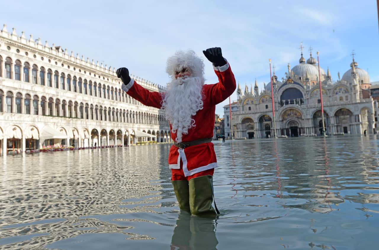epa08088328 A man disguised as Santa Claus poses in San Marco square flooded by high water, Venice, Italy, 23 December 2019. The high tide reached 144 cm.  EPA/Andrea Merola