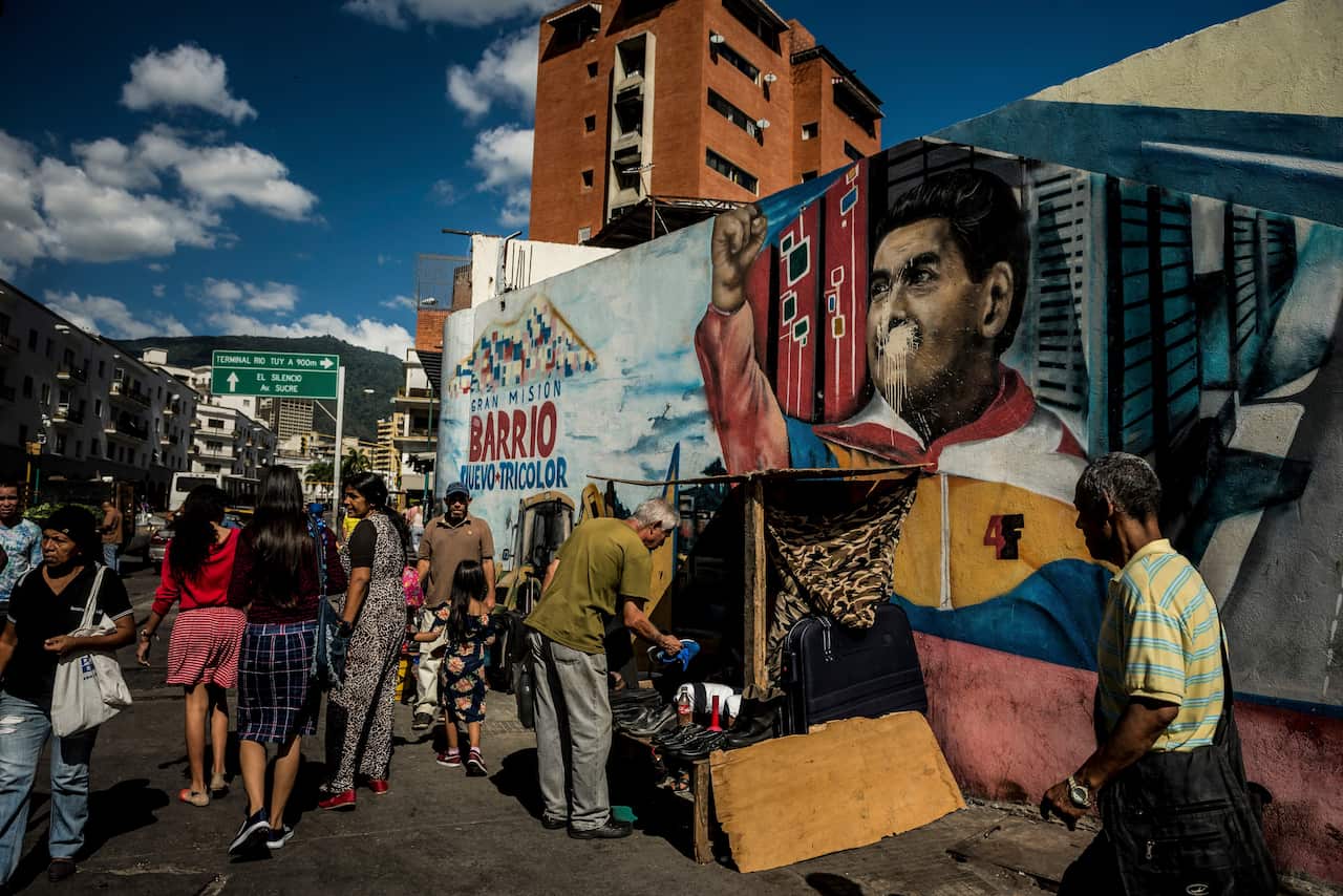 People pass a defaced mural of Venezuelan President Nicolas Maduro in the center of Caracas, Venezuela