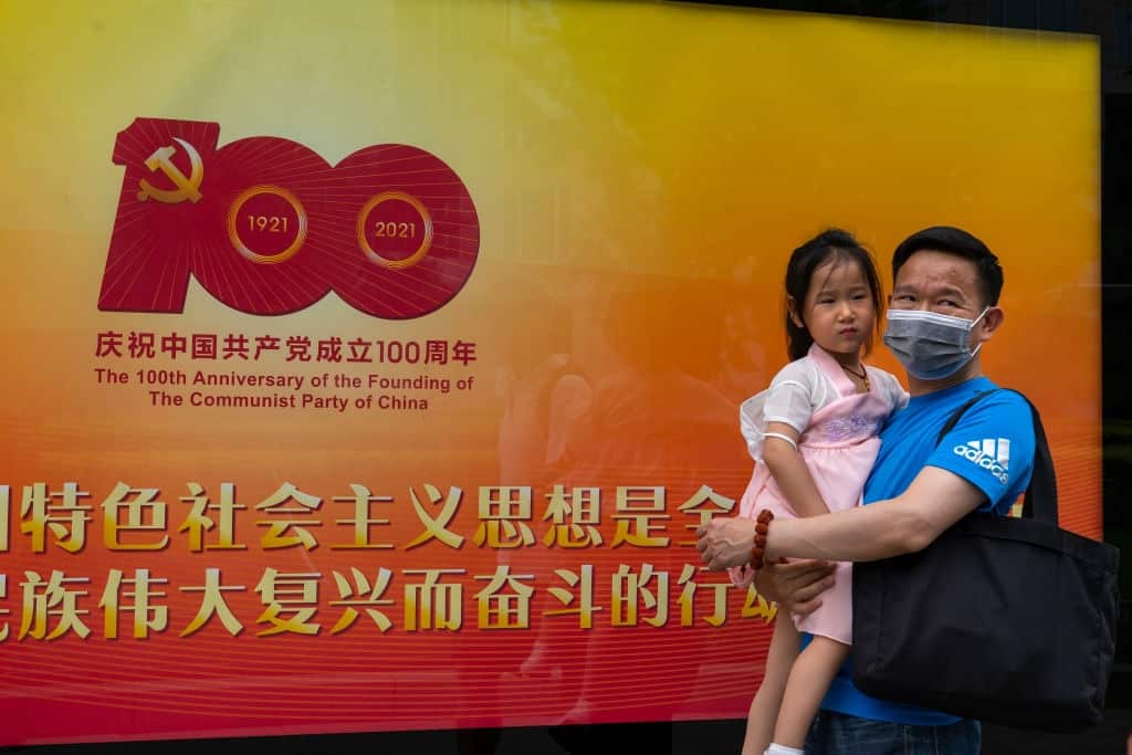 A man and child in front of a sign marking the centenery celebrations in Beijing. 