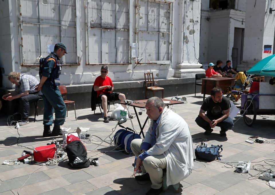People charge their electronic devices in front of a theatre building destroyed during Ukraine-Russia conflict in Mariupol, May 30 2022.