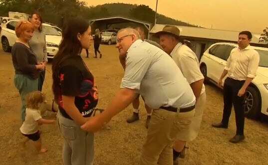 The prime minister reaches down to grab a woman's hand during a visit to bushfire-ravaged Cobargo. 