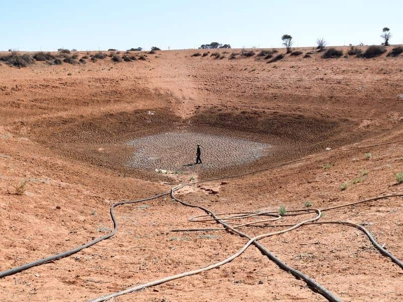 A farmer stands at the bottom of one of his empty dams