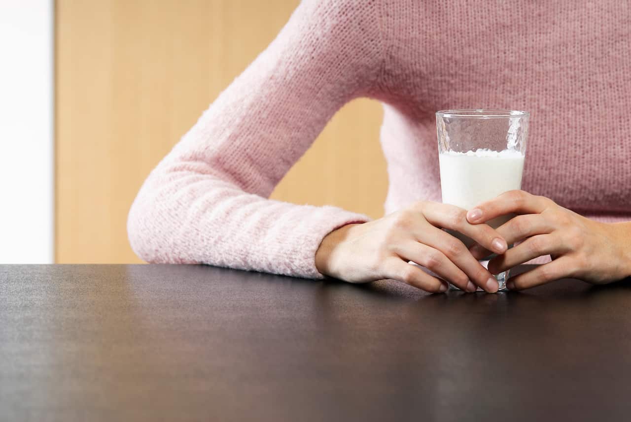 Woman holding glass of milk on table mid section