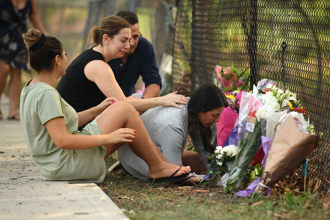A group pauses near flowers placed at the scene where seven children were hit by a four-wheel drive in the Sydney suburb of Oatlands.