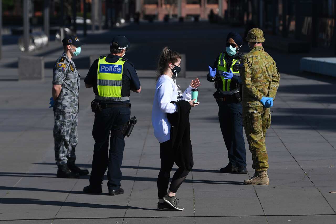 A person wearing a face mask walks past Victoria Police, Airforce and ADF personnel outside of the Melbourne Museum in Melbourne.