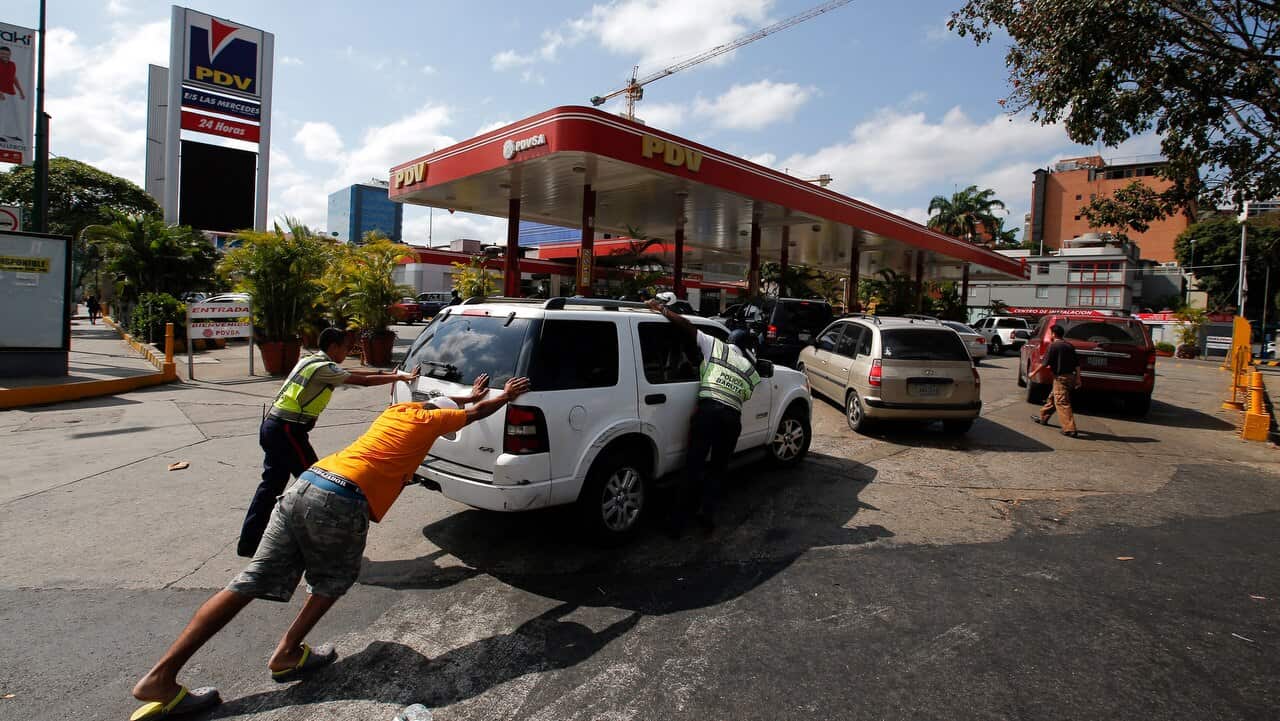 People push a car without gas to one of the few fuel stations that has its own electric generator during an electricity blackout in Caracas.