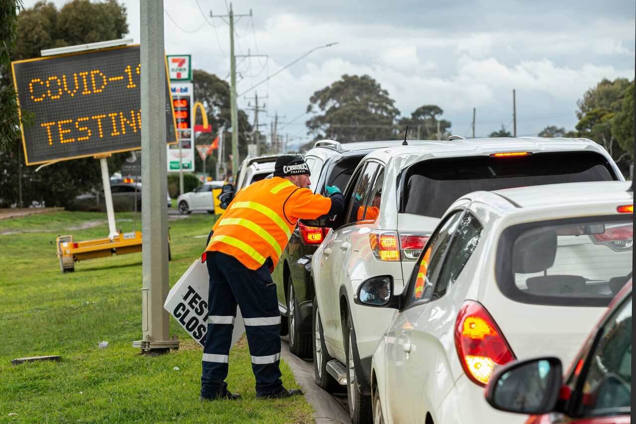 A man holding a sign saying testing closed directs cars outside a COVID-19 testing site at Craigieburn Health in Melbourne.