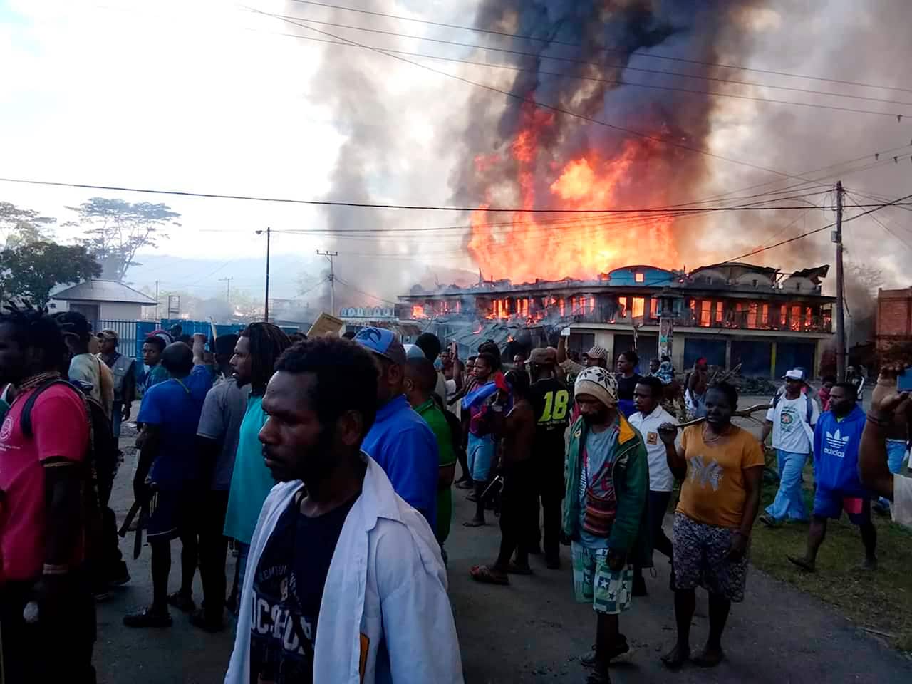 People gather as shops burn in the background during a protest in Wamena in Papua province, Indonesia, Monday, Sept 23, 2019. 
