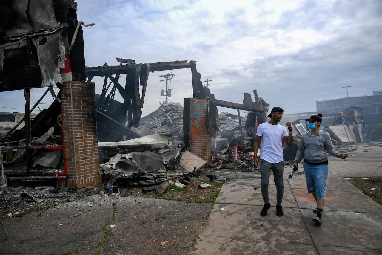 Pedestrians walk past destroyed buildings following riots over the death of George Floyd in the US.  