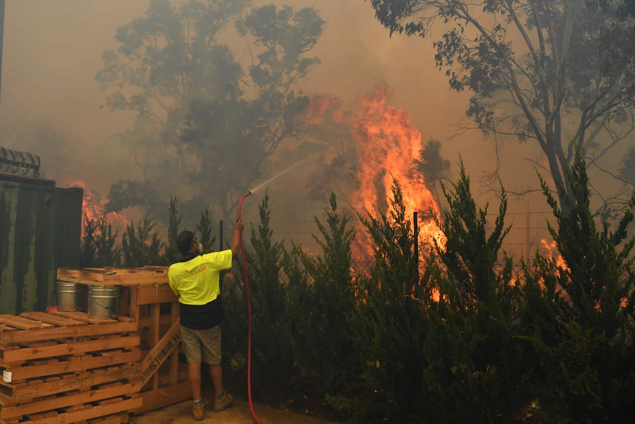Worker try to put out a bushfire behind a row of factories near West Queenbeyan, 10km west of Canberra.