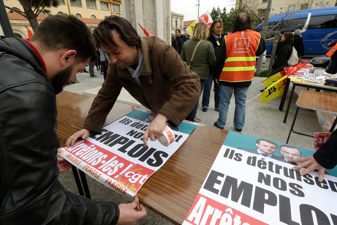 Rail workers stick posters reading "They kill our jobs, let's stop them".