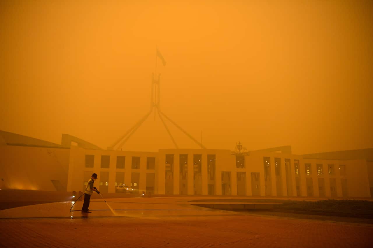 A man cleans the forecourt of Parliament House surrounded by smoke haze early morning in Canberra, Sunday, January 5, 2020. (AAP Image/Lukas Coch) NO ARCHIVING