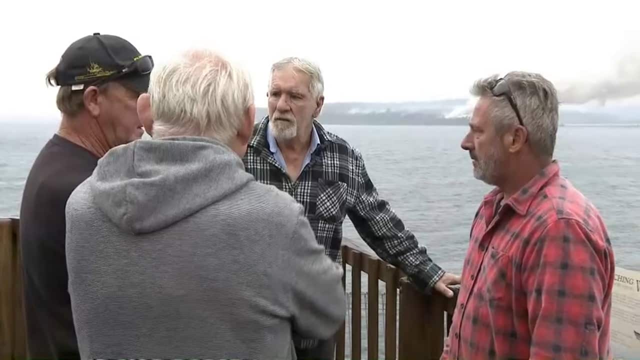 Peter with other locals in Eden watch the smoke from a large woodchip pile, near the local mill, which caught fire.