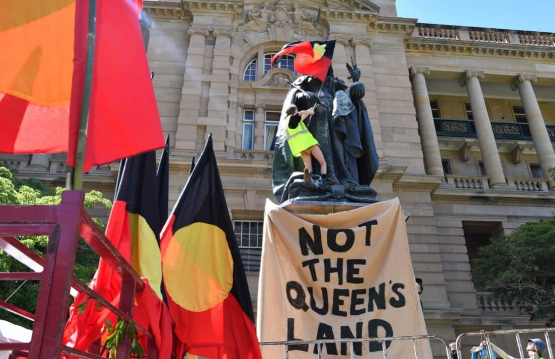 A protester attaches an Aboriginal flag to a statue of Queen Victoria during an 'Invasion Day' rally in Brisbane. 