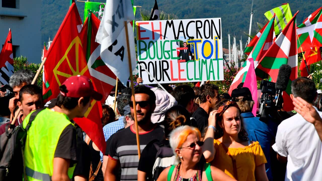 A protester holds a placard reading Hey Macron, get moving for the climate as other hold basque flags during a gathering in Hendaye, south-west France.