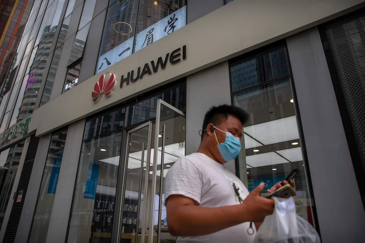 A man wearing a face mask to protect against the new coronavirus looks at his smartphone as he walks past a Huawei store in Beijing.