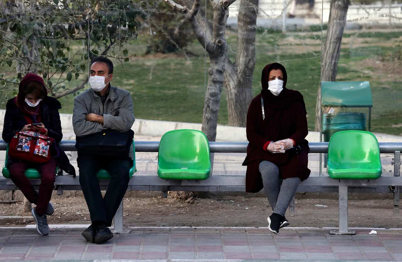 People wearing face masks wait for bus in a bus stop in a street in western Tehran, Iran.