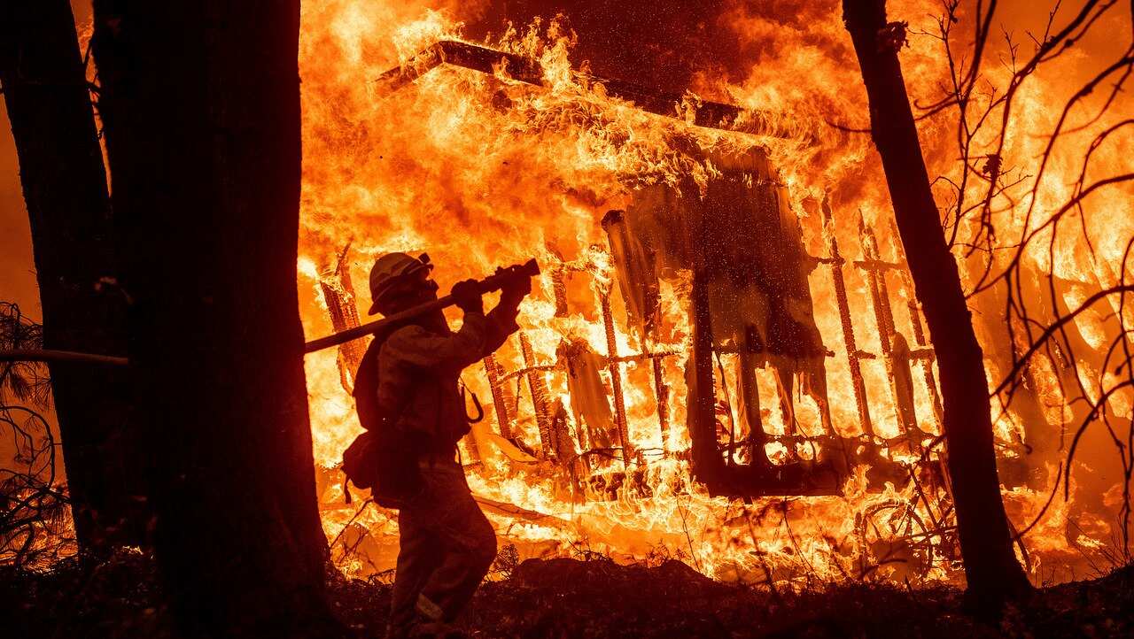 Firefighter Jose Corona sprays water as flames consume from the Camp Fire consume a home in Magalia, California.